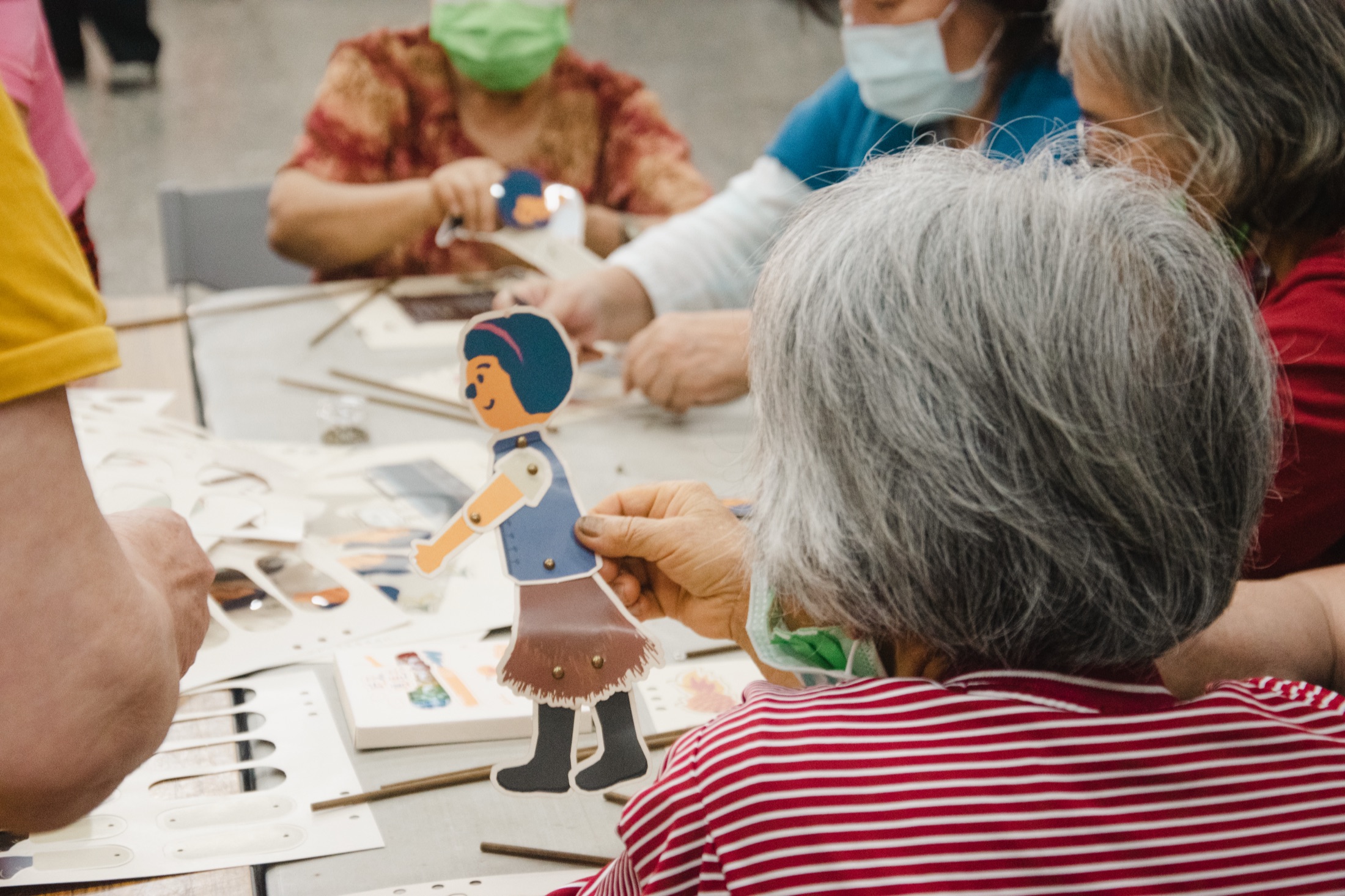 In-use detail — elderly participant holding completed puppet figurine
